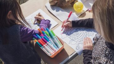 two young girls sitting at a table with markers and crayons