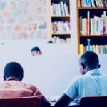 a couple of men sitting at a table in front of a book shelf