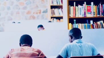 a couple of men sitting at a table in front of a book shelf